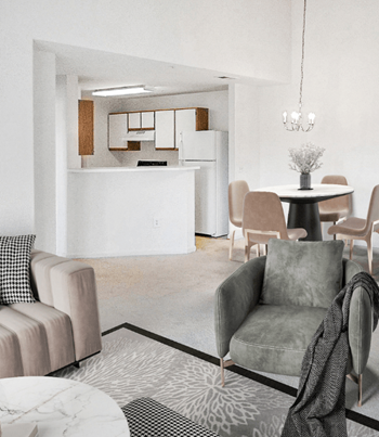 Vacant living room with tan carpet, white walls, and ceilings. The kitchen is in the background with a chandelier hanging over the dining area. Virtually staged with a couch, decorative chair, accent rug and coffee table, with dining table and four chairs in the background under the chandelier.